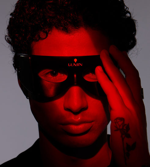 Man wearing black Lumin eye mask with red lighting highlighting facial features, curly hair, and hand tattoo visible.