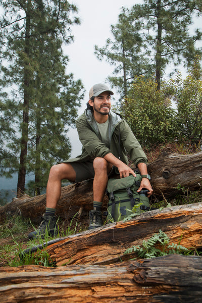 Smiling man in outdoor hiking gear sitting on a log in a forest setting.