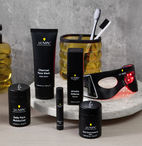 Luxury black skincare set with cleanser, body butter, serum, lip balm, and eye mask, displayed with toothbrush and amber jar on marble surface.