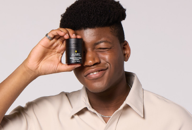 Smiling man holding a jar of men's skincare product close to his eye.