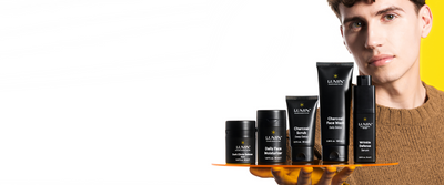 Male model holding a tray with Lumin men's skincare products: dark circle balm, moisturizer, charcoal scrub, face wash, and wrinkle serum.