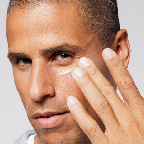 Man applying moisturizing eye cream under eye, close-up skincare routine for men, anti-aging facial care product