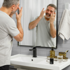 Middle-aged man applying anti-aging face cream in modern bathroom with skincare products on white sink counter.