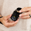 Hands holding Lumin Instant Dark Circle Corrector skincare bottle with beige corrector cream on finger
