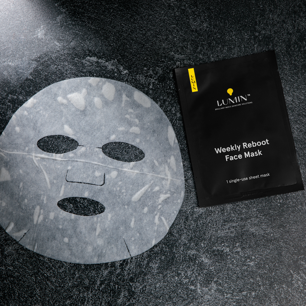 Lumin Weekly Reboot single-use men's sheet face mask with cutouts for eyes, nose, and mouth on textured black surface
