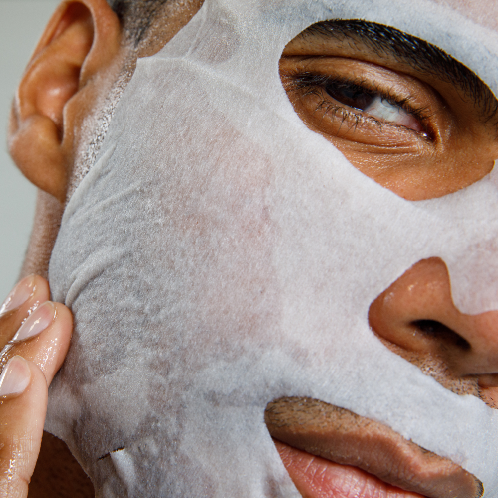 Man applying white hydrating facial sheet mask for skincare and self-care routine close-up